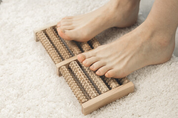 Woman massaging her feet with wooden roller foot massager. Self-massage for relaxing legs. Close up.