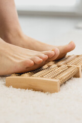 Vertical photo of Woman massaging her feet with wooden roller foot massager. Self-massage for relaxing legs. Close up.