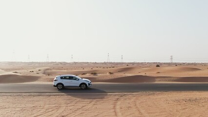 Vertical panning from a quadcopter. A white car is driving alone on a road in the desert. Aerial view of desert