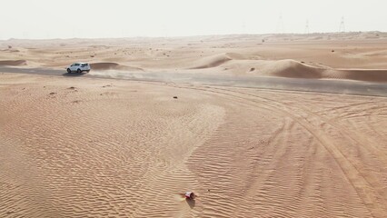 Vertical panning from a quadcopter. A white car is driving alone on a road in the desert. Aerial view of desert
