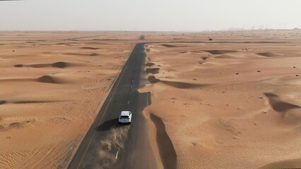 Vertical panning from a quadcopter. A white car is driving alone on a road in the desert. Aerial...