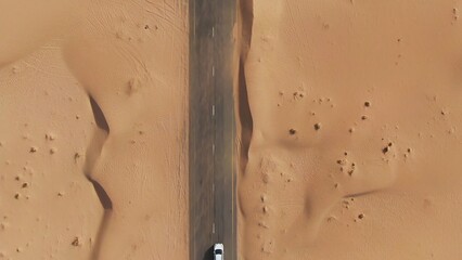 Vertical panning from a quadcopter. A white car is driving alone on a road in the desert. Aerial...