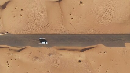 Vertical panning from a quadcopter. A white car is driving alone on a road in the desert. Aerial...