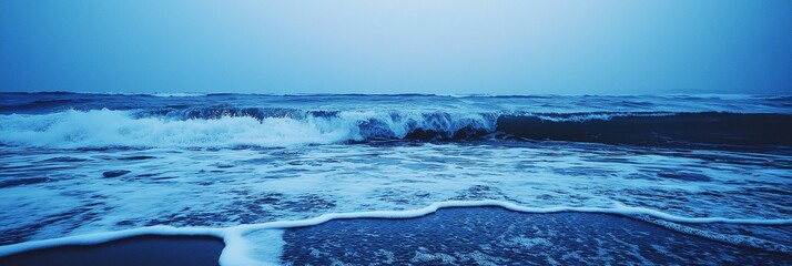 Fototapeta premium The ocean displays moody waves under a twilight-blue sky, creating a serene yet powerful atmosphere.