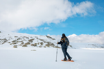 Female snowshoer hiking toward a snow-covered ridge in Sierra de Gredos, Spain, with trekking poles...