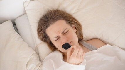Woman in Bed Forcefully Tearing Off Black Mouth Tape with Painful Expression While Lying in White...