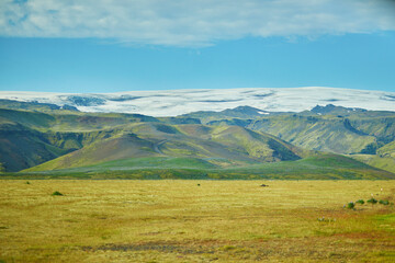 Beautiful nature landscape with green fields and majestic cliffs with ice and snow in Southern Iceland.