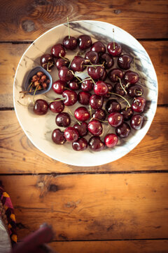 White bowl of cherries and pips on wood table