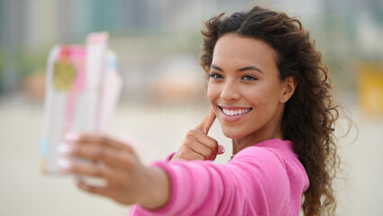 Happy young woman takes selfie with smartphone for social media outdoors. Picture of influencer lifestyle, sharing moments online and digital connection. Joy of modern communication. 
