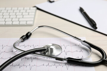 Cardiology. Stethoscope, cardiogram, keyboard, clipboard and pen on light table, closeup