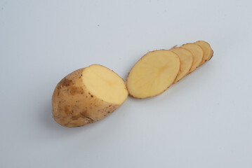 This image shows a fresh potato that has been partially sliced into thin, even rounds. The potato’s skin is light brown and slightly rough, while the inside is a pale yellow, indicating its freshness 