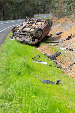 Crashed vehicle upside down on side of highway