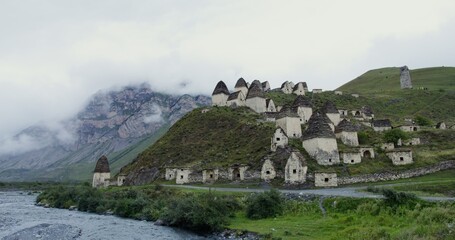 An ancient city of white brick towers on the hills near a seething mountain river, at the foot of rocky mountains, covered with thick clouds.