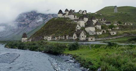 An ancient city of white brick towers on the hills near a seething mountain river, at the foot of rocky mountains, covered with thick clouds.