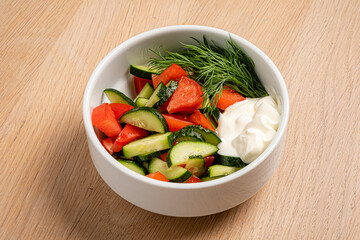 A vibrant bowl filled with crisp cucumbers and tomatoes alongside a dollop of creamy dressing