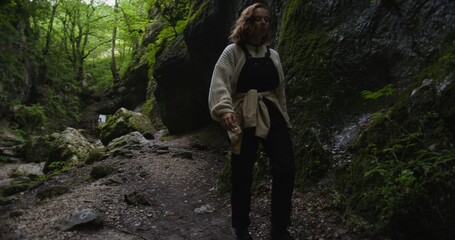 Russia, Caucasus. A beautiful young woman of European appearance walks along a narrow mountain path next to a mountain stream between sheer cliffs. The beauty of the Caucasian nature