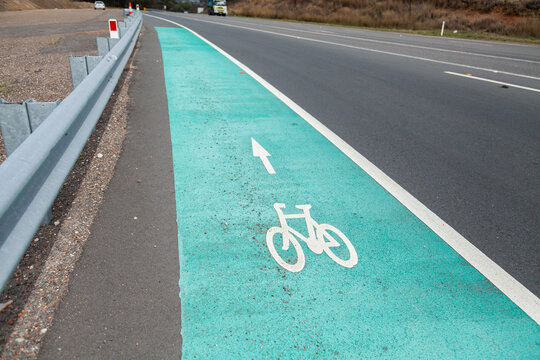 Green cycle path beside highway with bike and arrow sign