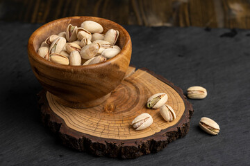 pistachio in shells with added salt, fried unpeeled pistachio nuts in a wooden bowl with cracked shell, close up