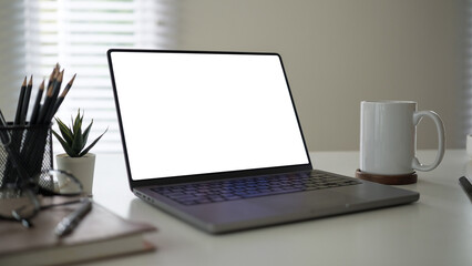 Fototapeta premium Modern desk setup featuring a laptop with a blank white screen, perfect for customization.