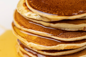 drizzled with honey, a large number of delicious pancakes stacked together on a white bowl, side view