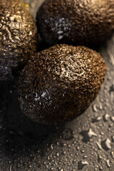 several wet whole black avocado fruits of small size on a black slate