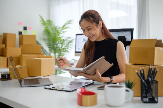 Casual businesswoman working efficiently with shipping boxes, stationery, and a laptop, illustrating an organized e-commerce business setup.