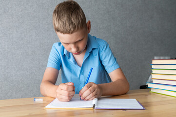 Naklejka premium Young Boy Concentrating on Writing Homework in Notebook. International Left Handers Awareness Day