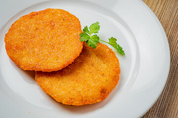 Two crispy, golden plantain fritters on a white plate, garnished with fresh cilantro