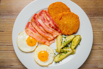 A delicious breakfast plate featuring crispy bacon, eggs, and golden hash browns with pickles