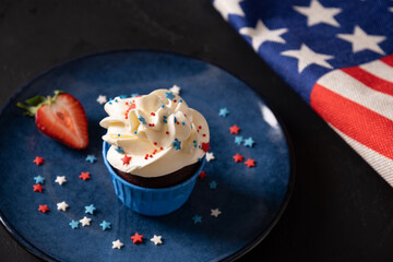 Traditional American sweet cupcake with sugar sprinkles as stars and USA flag in blue plate on dark background. Dessert for Patriotic Independence Day 4th of july. Close up.