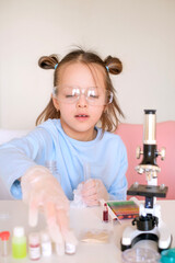 A preschool-age girl wearing gloves and safety glasses does a scientific experiment with mixing...