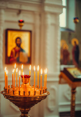Golden candle holder with burning Easter candles in Orthodox church interior with blurred religious icons on the background