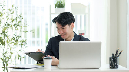 Businessman smiling while checking paperwork in a well-lit workspace.