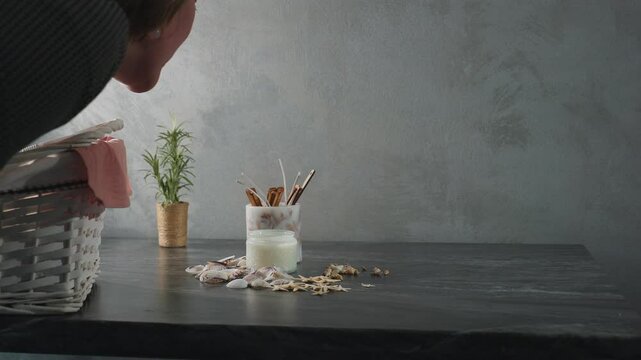 Woman blows out candle on dark marble table decorated with seashells, starfish, snail shells, and natural decor items as smoke rises