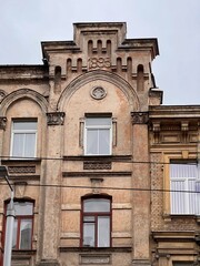 Old building in need of renovation. 1895 year of construction Arched windows with white frames are set within a faded, light-brown stucco exterior. 