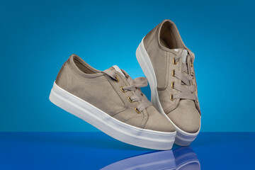 Stylish beige canvas sneakers, floating against a blue background with a glossy reflective surface. Modern footwear concept for fashion, e-commerce, and advertising