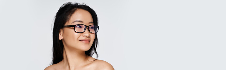Young Asian woman wearing glasses gazes with a gentle smile, embodying grace and beauty