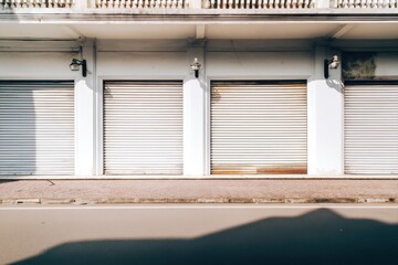 Fototapeta premium White closed roller shutter doors on the side of an empty street in the town center