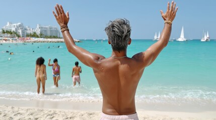 Man is standing on the beach with his arms raised, and there are several other people in the background. Scene is joyful and relaxed, as everyone is enjoying their time at the beach