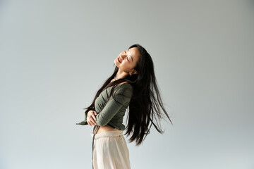 Young asian woman joyfully embracing the moment with flowing hair in a minimalist space
