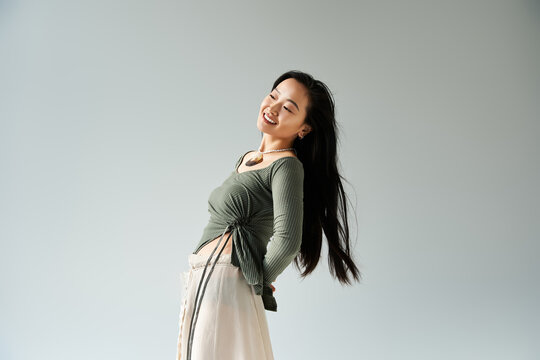 Young woman with long hair joyfully posing against a simple background in a stylish outfit