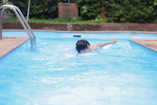 Healthy Asian man swimming freestyle in a stunning blue pool under the bright sun, enjoying a refreshing vacation while training for upcoming competitions and enhancing his fitness