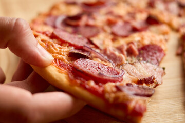Close up of a hand reaching for a slice of pepperoni pizza. The golden crust is topped with melted cheese, savory pepperoni, and herbs, enhancing its flavor