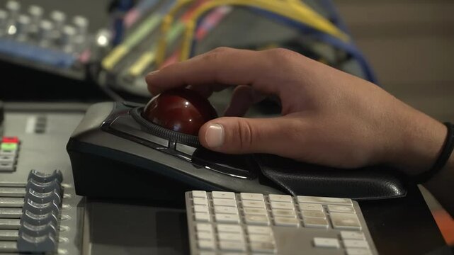 Close-up of a hand manipulating audio equipment, specifically a mixing console and trackball mouse, in a professional studio setting.