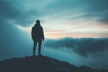 A lone figure stands on a mountain peak, gazing at a dramatic sunset, representing solitude and reflection.