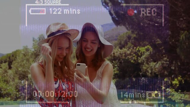 Laughing and looking at smartphone, two women in sun hats with animation