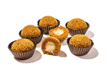 Honey balls in brown wrapper and next to it cut in half with milk filling on white background. Candies on white background.