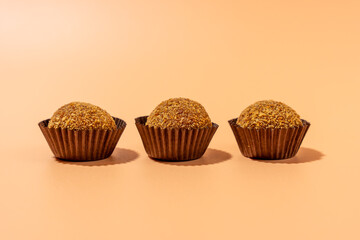 Three brown cupcakes are sitting on a table. They are all the same size and shape. The cupcakes are in brown paper cups