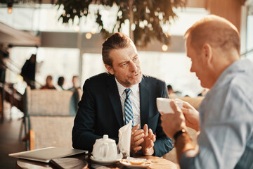 Businessmen having serious conversation over coffee in modern cafe
