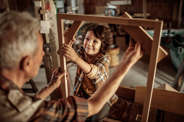 Grandfather teaching grandson woodworking in home workshop
